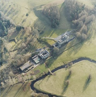 Oblique aerial view centred on the country house with stables and bridge adjacent, taken from the NNE.