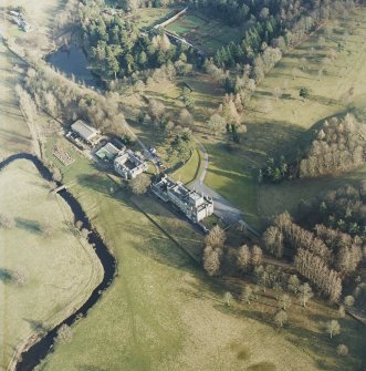 Oblique aerial view centred on the country house with stables, greenhouse and bridge adjacent, taken from the NW.