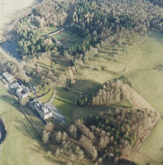 Oblique aerial view centred on the country house with stables and greenhouse adjacent, taken from the NW.
