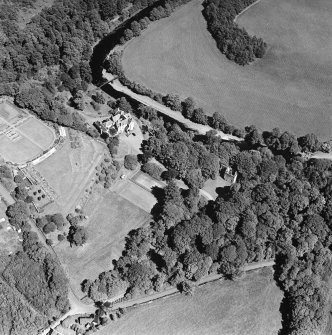 Oblique aerial photograph of Knockdolian Castle taken from the SW, centred on the country house and policies with the tower house in the trees.