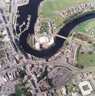 Oblique aerial view centred on the boatbuilding yard and harbour, with the burial-ground adjacent, taken from the ESE.