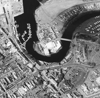 Oblique aerial view centred on the boatbuilding yard and harbour, with the burial-ground adjacent, taken from the WSW.