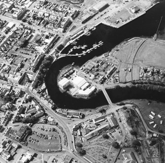 Oblique aerial view centred on the boatbuilding yard and harbour, with the burial-ground adjacent, taken from the WNW.