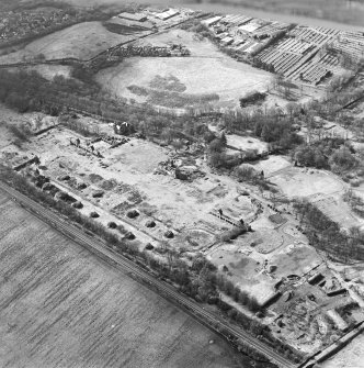 Oblique aerial view centred on the remains of the former hospital, the east and west corridor links of the hospital, the west wing, the east wing, and church, taken from the ESE.