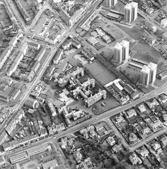 Oblique aerial view centred on the hospital and churches, taken from the NW.