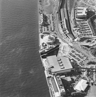 Oblique aerial view centred on the harbour and the Discovery visitor centre, with the leisure centre and railway station adjacent, taken from the NE.