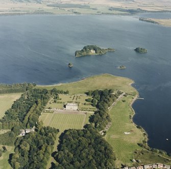 Oblique aerial view of Kinross House centred on the country house with garden and stables, and with a church, burial ground and castle in the background, taken from the W.