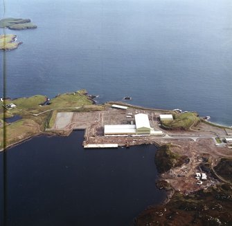 Oblique aerial view centred on the oil rig construction yard with the lighthouse and the remains of the coast battery adjacent, taken from the NW.