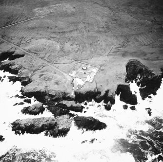 Oblique aerial view centred on the lighthouse with the remains of the enclosures adjacent, taken from the N.