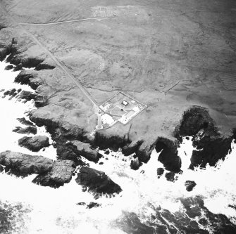 Oblique aerial view centred on the lighthouse with the remains of the enclosure adjacent, taken from the NNW.