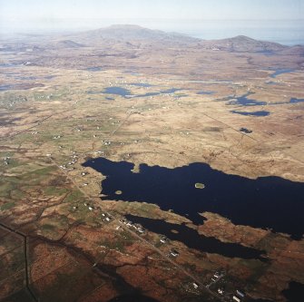 General oblique aerial view looking across the township and the remains of the dun towards Dalabrog, and Beinn Mhor in the distance, taken from the SW.