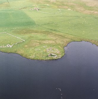 Oblique aerial view centred on the remains of the broch with the remains of the buildings, burnt mound and croft buildings adjacent, taken from the SW.