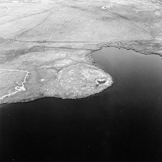 Oblique aerial view centred on the remains of the broch with the remains of the buildings and burnt mound adjacent, taken from the W.