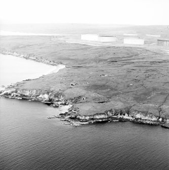 Oblique aerial view centred on the remains of the coast battery with the oil pipeline terminal adjacent, taken from the WSW.