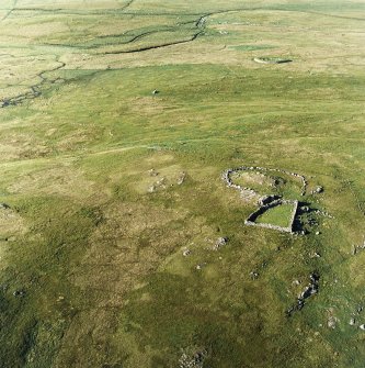 Oblique aerial view centred on the remains of the cairns and stock enclosures with the remains of the ritual building, field-system and standing stones adjacent, taken from the SW.
