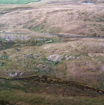 Oblique aerial view centred on the remains of the building, planticrubs, enclosures and quarries, taken from the SSW.