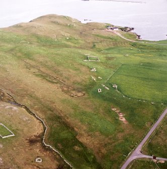 Oblique aerial view centred on the remains of the enclosures and buildings with the remains of the planticrub, enclosure and quarries adjacent, taken from the NW.