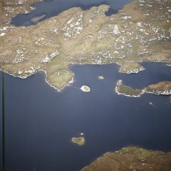 Oblique aerial view centred on the remains of the broch with the causeway adjacent, taken from the WSW.