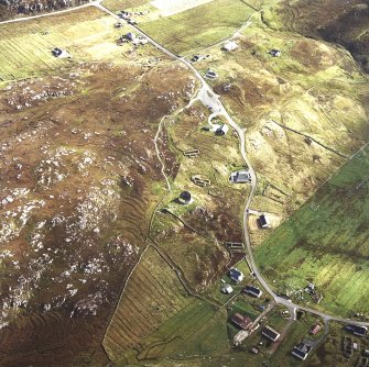 Oblique aerial view centred on the remains of the broch with the remains of the blackhouse and township adjacent, taken from the WNW.