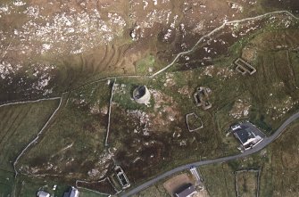 Oblique aerial view centred on the remains of the broch with the remains of the blackhouse and township adjacent, taken from the SW.