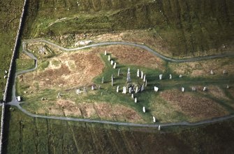 Lewis, Callanish. Oblique aerial view centered on the remains of the stone circle, stone alignments and chambered cairn, taken from the ESE.