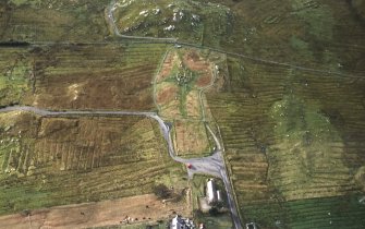 Oblique aerial view centred on the remains of the stone circle, chambered cairn and stone alignments with the blackhouse and lazy beds adjacent, taken from the NNE.