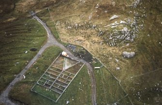 Oblique aerial view centred on the reconstructed shieling hut and sheep pen, taken from the NNW.