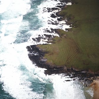 Oblique aerial view centred on the remains of the dun and building with the remains of lazy beds adjacent, taken from the SW.