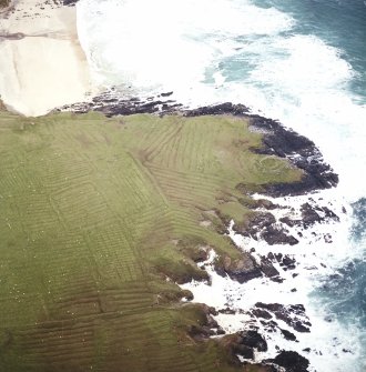 Oblique aerial view centred on the remains of lazy beds with the remains of the dun and building adjacent, taken from the NE.