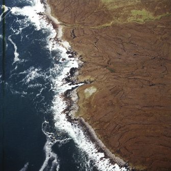 Oblique aerial view centred on the remains of the chambered cairn, taken from the WSW.