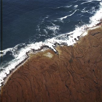 Oblique aerial view centred on the remains of the chambered cairn, taken from the SSW.