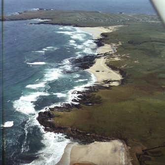 General oblique aerial view looking across the remains of the dun, building and the lazy beds along the west coast of Lewis towards Eoropie, taken from the SW.