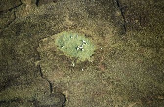 Oblique aerial view centred on the remains of the chambered cairn, taken from the WSW.