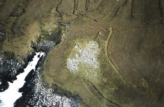 Oblique aerial view centred on the remains of the chambered cairn, taken from the NW.