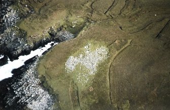 Oblique aerial view centred on the remains of the chambered cairn, taken from the WNW.