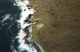 Oblique aerial view centred on the remains of the chambered cairn, taken from the WSW.