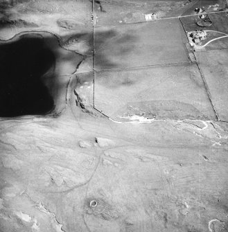 Oblique aerial view centred on the remains of the hut-circles, farmstead and rig with the hotel adjacent, taken from the WNW.