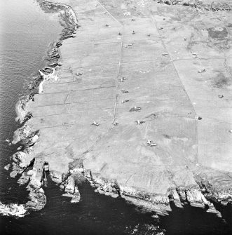Stroma, oblique aerial view, taken from the E, centred on Uppertown township. A dovecot and burial ground, and the remains of Fendie Clett castle are visible in the bottom left-hand corner of the photograph.