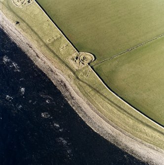 Oblique aerial view centred on the remains of the broch with the possible building and pillbox adjacent, taken from the ENE.