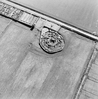 Oblique aerial view centred on the remains of the broch with the memorial and graveyard adjacent, taken from the NW.