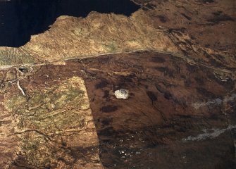 Oblique aerial view centred on the remains of the chambered cairn, taken from the SW.