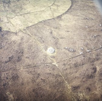 Oblique aerial view centred on the remains of the chambered cairn, taken from the NE.