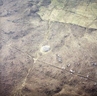 Oblique aerial view centred on the remains of the chambered cairn, taken from the NNW.