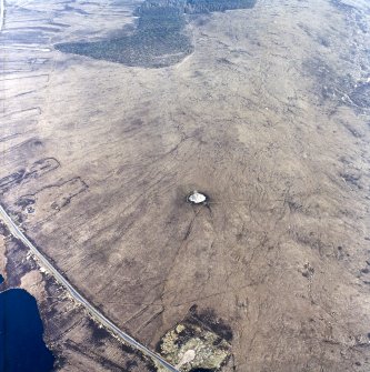 Oblique aerial view centred on the remains of the chambered cairn, taken from the WNW.