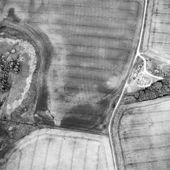 Oblique aerial view centred on the cropmarks of the possible enclosure, roundhouse, rig and pits with cottages adjacent, taken from the SW.