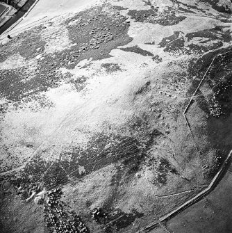 Oblique aerial view centred on the remains of the cairn and small cairns with buildings adjacent, taken from the SSE.