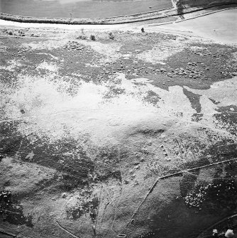 Oblique aerial view centred on the remains of the cairn and small cairns with buildings adjacent, taken from the SE.