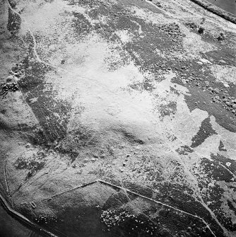 Oblique aerial view centred on the remains of the cairn and small cairns with buildings adjacent, taken from the E.