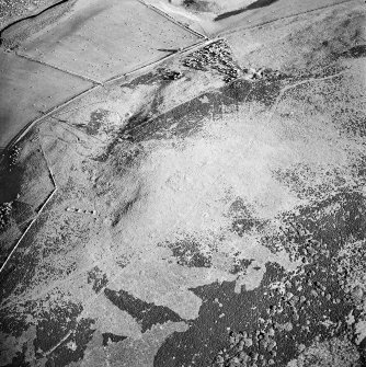 Oblique aerial view centred on the remains of the cairn and small cairns with buildings adjacent, taken from the NNW.
