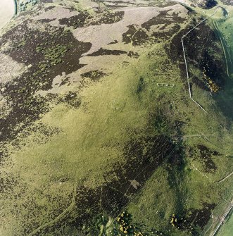 Oblique aerial view centred on the remains of the cairn and small cairns with buildings adjacent, taken from the SSW.